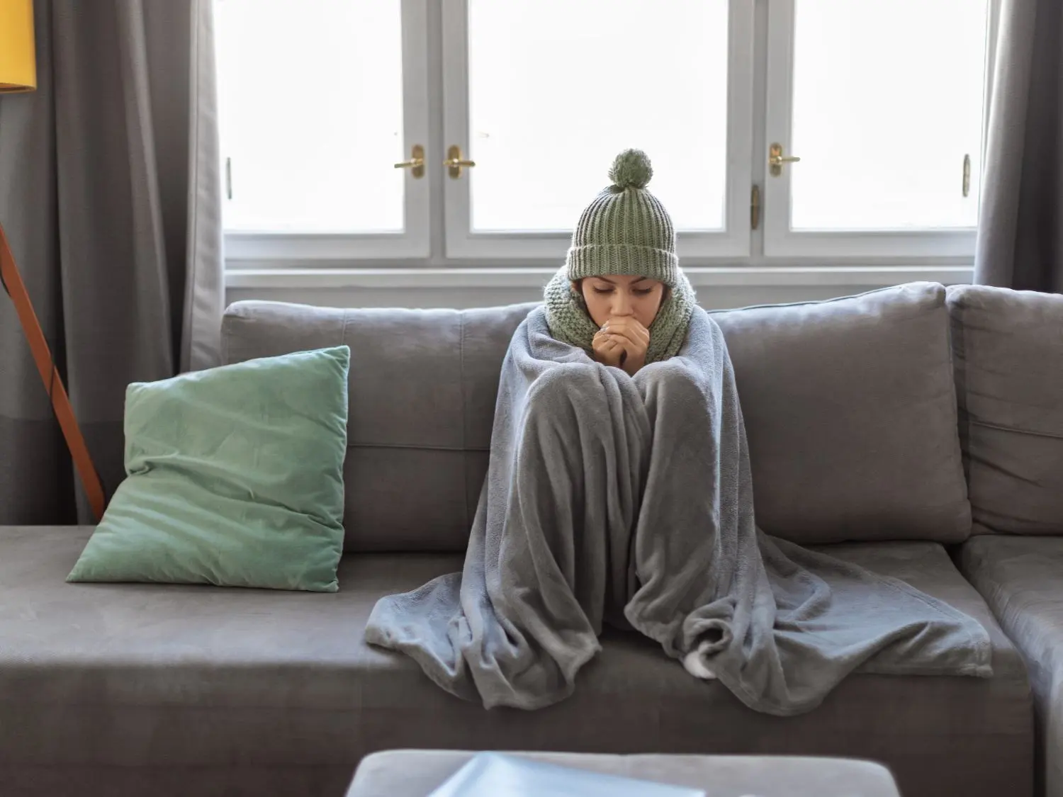Woman huddling under a blanket while sitting on a couch