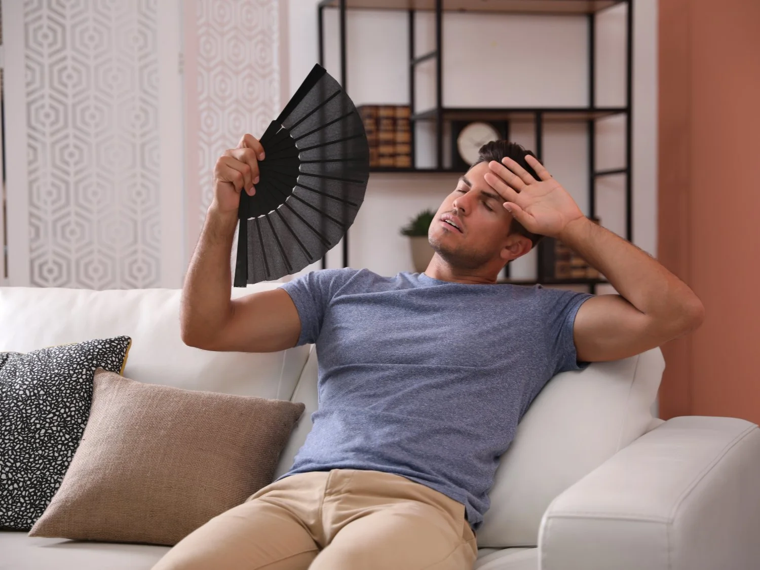 Hot man using fan while sitting on couch